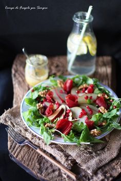 a salad with apples, radishes and walnuts on a plate next to a jar of lemonade