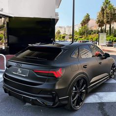 the rear end of an audi car parked in a parking lot with palm trees behind it