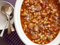 a white bowl filled with pasta and meat soup next to a spoon on a purple checkered table cloth