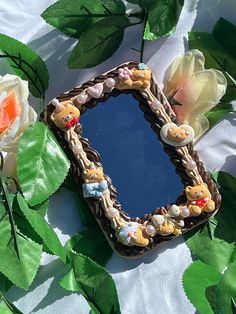 a decorative mirror sitting on top of a table next to some flowers and green leaves