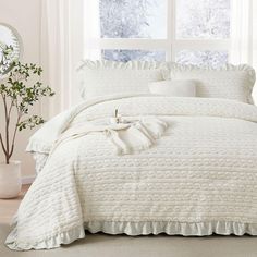 the comforter is white and has ruffles on it, along with pillows