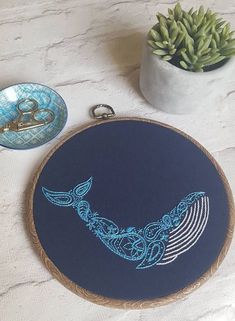 an embroidered whale on a blue background next to scissors and a potted plant with succulents