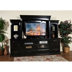 a black entertainment center with a television on it's side and plants in the corner