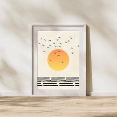 an art print with birds flying over the ocean at sunset, on a wood floor