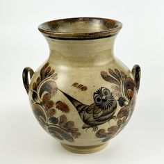 a vase with an owl painted on the side and leaves around it, sitting on a white surface