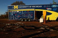 a man standing next to a yellow and blue truck with michigan university on the side