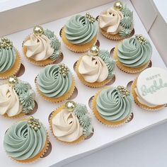 twelve cupcakes with frosting and gold decorations in a white box on a table