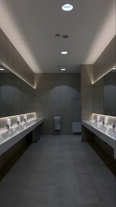 an empty public restroom with sinks and mirrors on the walls, lights above them are recessed in concrete