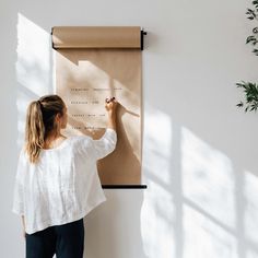 a woman writing on a piece of paper while standing next to a wall mounted plant