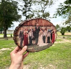 a hand holding up a piece of wood with an image of people on it in front of some trees