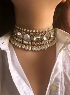 a close up of a woman wearing a white shirt and gold choker with pearls on it