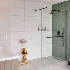 a bathroom with a glass shower door and white tiles on the walls, along with a wooden stool