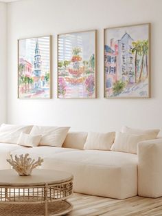 a living room with white furniture and paintings on the wall above it's coffee table