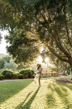 a woman is walking through the grass in front of a large tree and some bushes