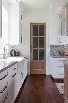 a kitchen with white cabinets and wood floors, along with a wooden door that leads to another room