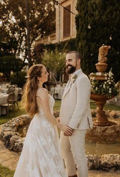 a bride and groom holding hands in front of a fountain at their wedding reception outside