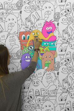 a woman is drawing on a wall with colorful cartoon characters in the background and behind her