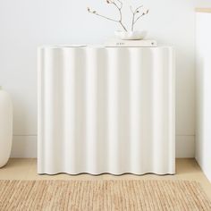 a white cabinet sitting on top of a rug next to a vase with flowers in it