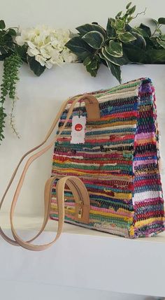 a multicolored purse sitting on top of a white shelf next to some flowers