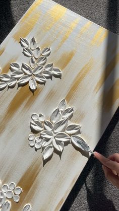 someone is using a brush to paint on a piece of wood that has been painted gold and white