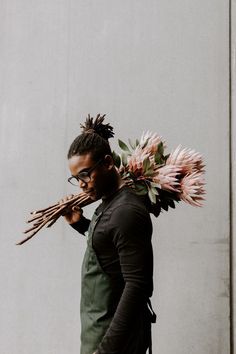 a man with flowers on his head walking down the street while carrying something in his hand