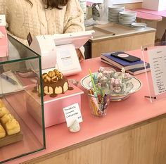 a woman standing behind a counter filled with pastries and desserts on display in front of her