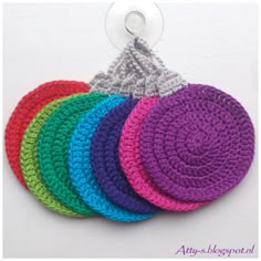 four crocheted coasters in different colors on a white background with a metal hook