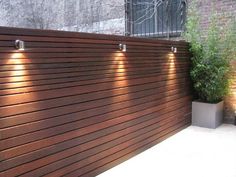 a wooden fence with three lights on it and a potted plant next to it