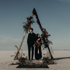 a man and woman standing in front of an arch made out of branches with flowers