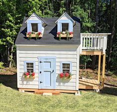 a small house with two windows and flowers on the roof, next to a deck