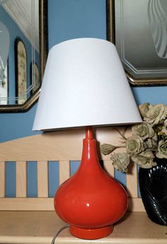 a red lamp sitting on top of a wooden table next to a vase with flowers