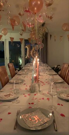 a table set for a birthday party with candles and balloons in the air above it