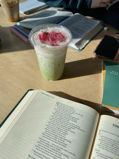 an open book sitting on top of a wooden table next to a cup of drink