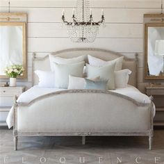 a white bed sitting under a chandelier next to two mirrors on the wall