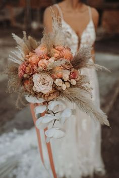 a woman in a white dress holding a bridal bouquet with flowers and feathers on it