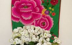 a hand holding a can filled with flowers next to a wall hanging on a wall