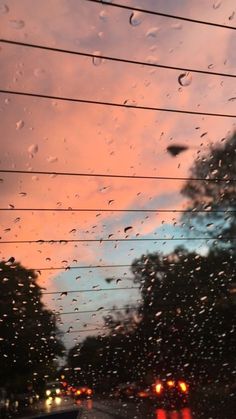 rain drops on the windshield of a car as it drives down a street at dusk