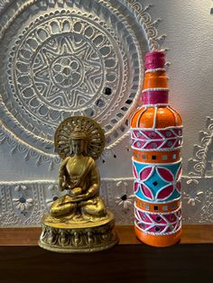 a buddha statue next to an orange and blue bottle on a wooden table in front of a white wall