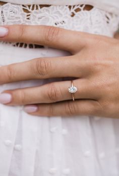 a woman's hand with a diamond ring on her left hand and a white lace dress