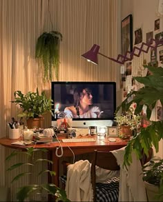 a desk with a computer, plants and pictures on the wall