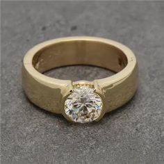 a yellow gold ring with a diamond in the center on a gray surface, close up