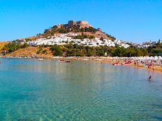 people are swimming in the clear blue water near an island with white buildings on it