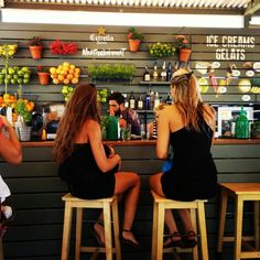 three women sitting at a bar in front of shelves with fruits and vegetables on them