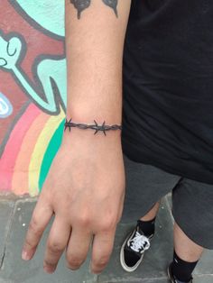 a man with a tattoo on his arm and hand is wearing a barbed wire bracelet