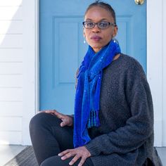 a woman sitting in front of a blue door with her hands on her hips and looking at the camera