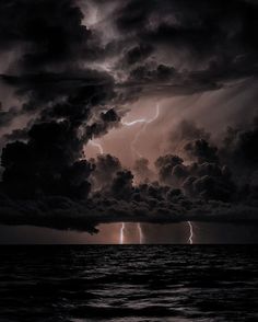 the sky is filled with dark clouds as lightning strikes in the distance over the ocean