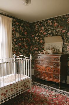 a white crib sitting next to a window in a room with floral wallpaper