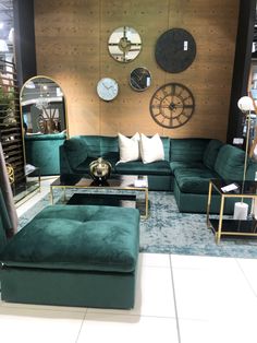 a living room filled with green couches and clocks on the wall behind them in a store