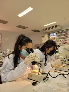 two women in lab coats looking through microscopes