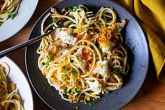 a plate of spaghetti with meat and parmesan cheese on top, next to two plates of pasta